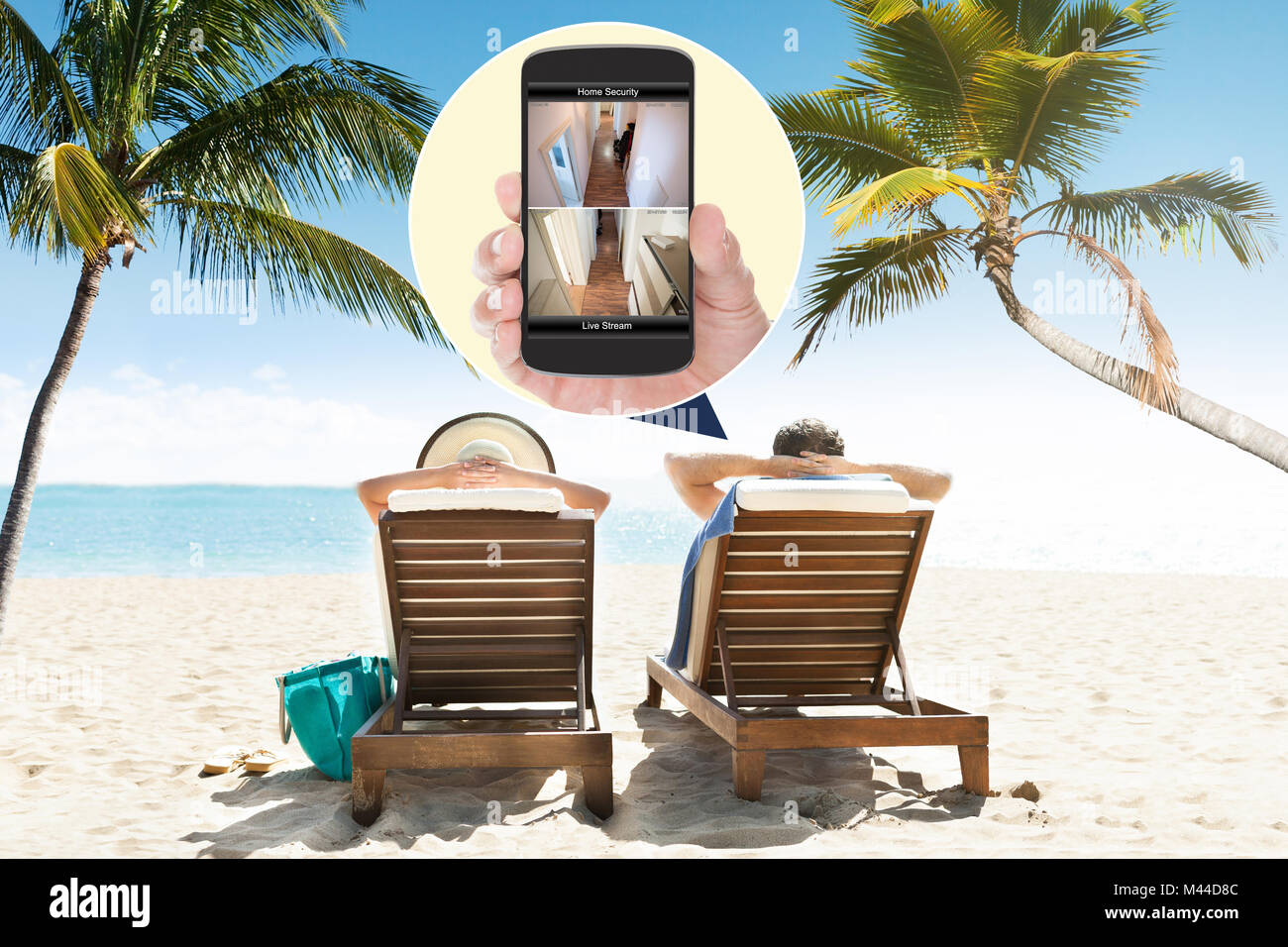 Paar sitzt auf Liegestuhl am Strand mit Home Sicherheit Kameras gesehen auf dem Mobiltelefon Stockfoto