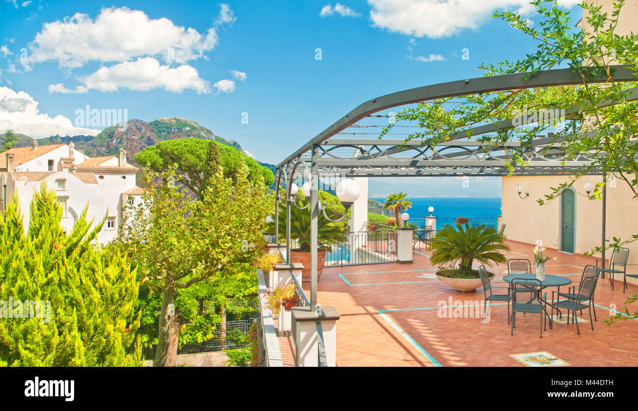 Panorama von der Terrasse mit Tisch und Blumen in Villa mit Blick auf Meer und Berge auf der sonnigen Sommertag in Ravello, Amalfi Küste Stockfoto