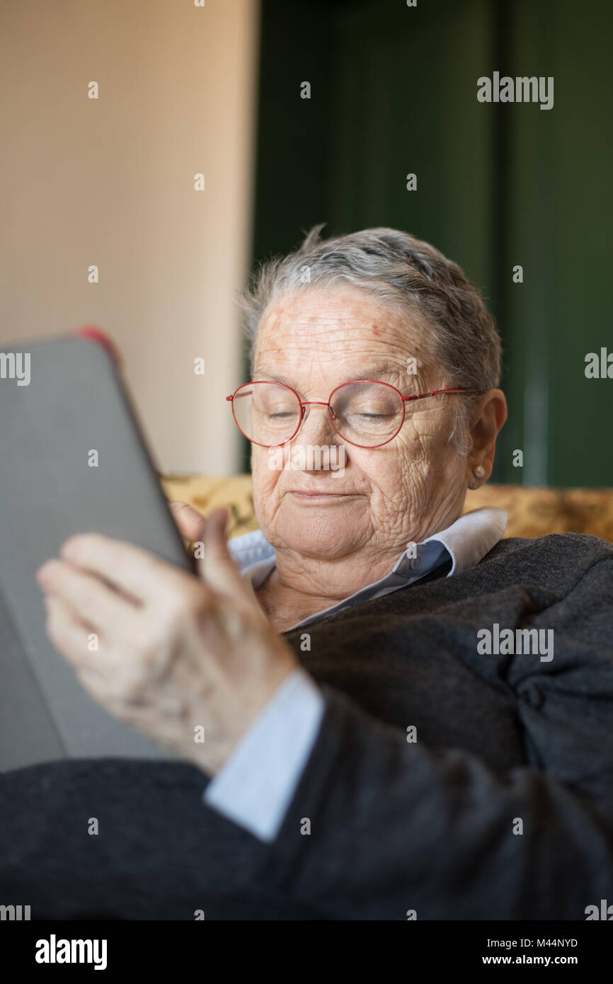 Ältere Frau zu Hause auf dem Sofa sitzen mit Tablet e-Buch portrait selektiven Fokus auf dem Gesicht Stockfoto