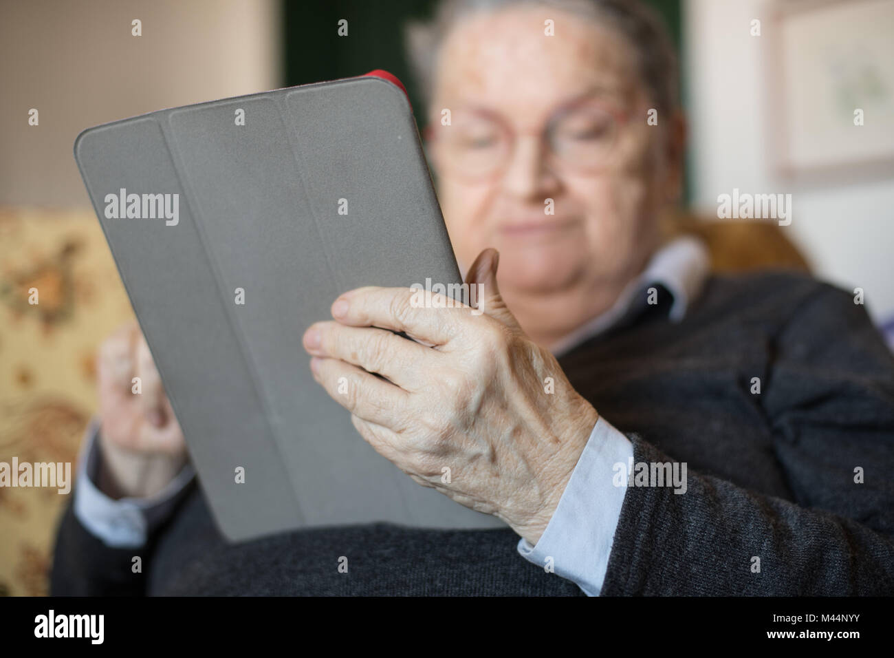 Ältere Frau zu Hause auf dem Sofa sitzen mit Tablet e-Buch portrait selektiven Fokus auf Händen Stockfoto