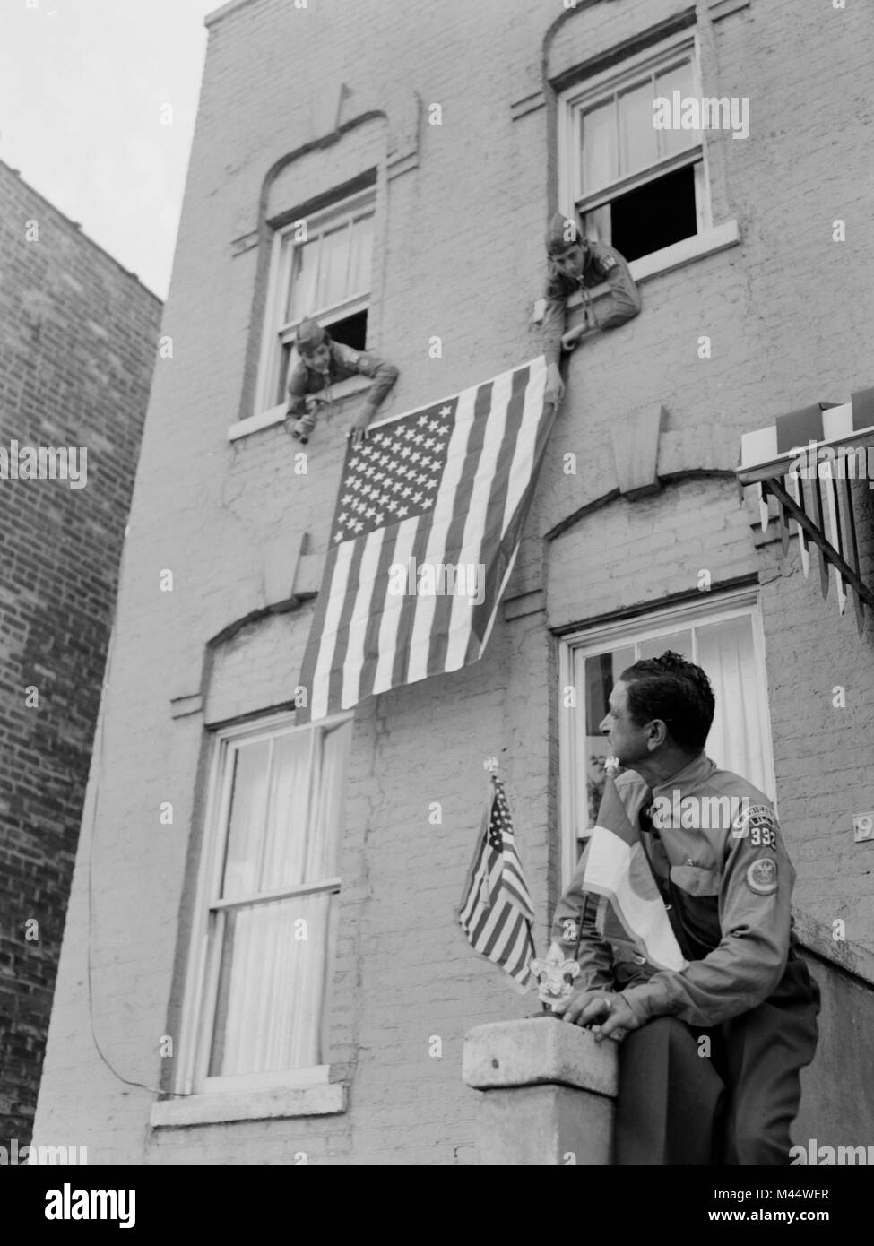 Pfadfinder hängen uns Flaggen aus dem Fenster eines Chicago Gebäude, Ca. 1960. Stockfoto