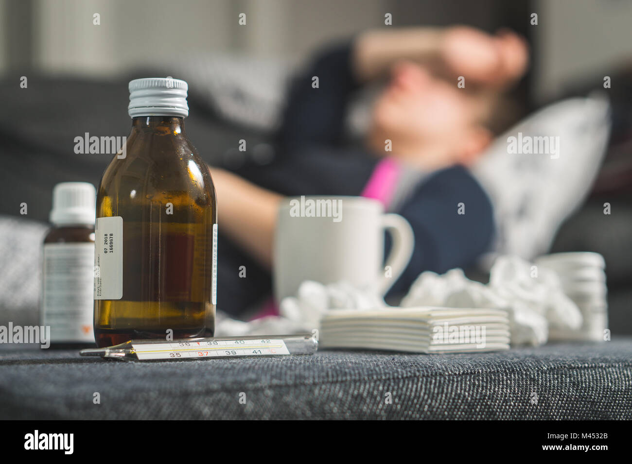 Kranke Frau mit Kopf und Stirn mit der Hand und des Arms. Medizin, Thermometer, heißes Getränk und verschmutzte Papierhandtücher in Front. Person mit Grippe. Stockfoto