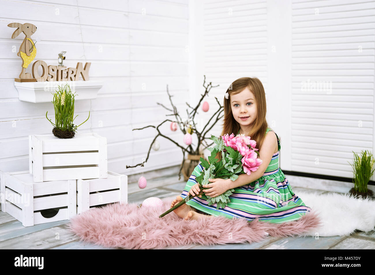 Vier Jahre altes Mädchen mit rosa Blumen in den Händen auf weißem Hintergrund Rund um Ostern Dekorationen Stockfoto