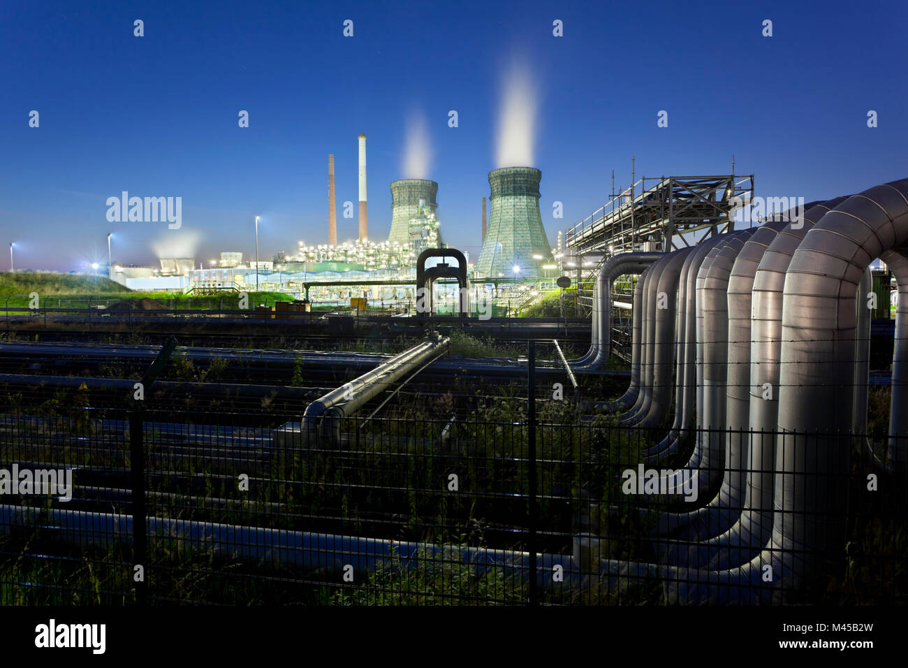 Eine Ölraffinerie mit zwei Kühltürme und blauen Nachthimmel, viele Pipelines in den Vordergrund. Stockfoto