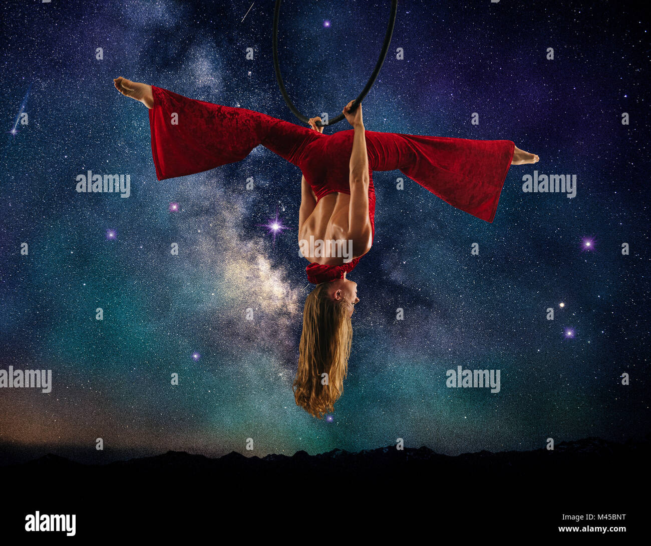 Junge weibliche Antenne Acrobat tun Splits hängt kopfüber von Hoop, Milchstraße Hintergrund Stockfoto