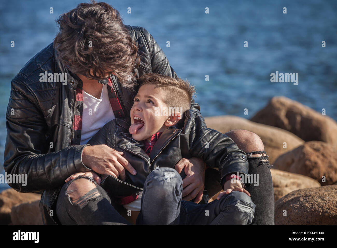Vater und Sohn im Freien, um zu täuschen, sitzen auf den Felsen neben dem Meer Stockfoto