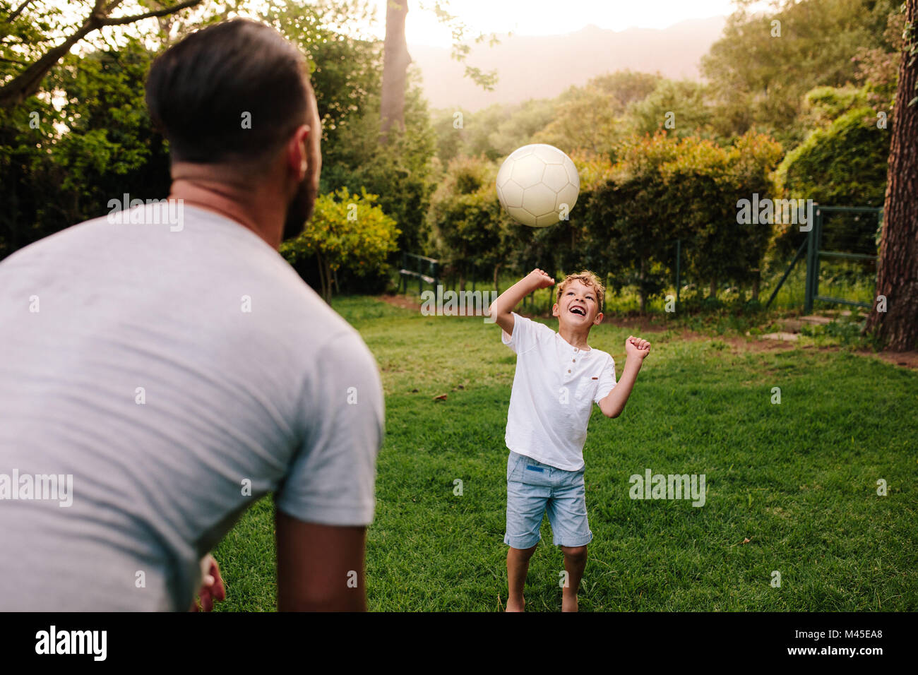 Vater und Sohn spielen mit einem Fußball im Garten im Hinterhof. Happy little boy, die Kugel zu seinem Vater. Stockfoto