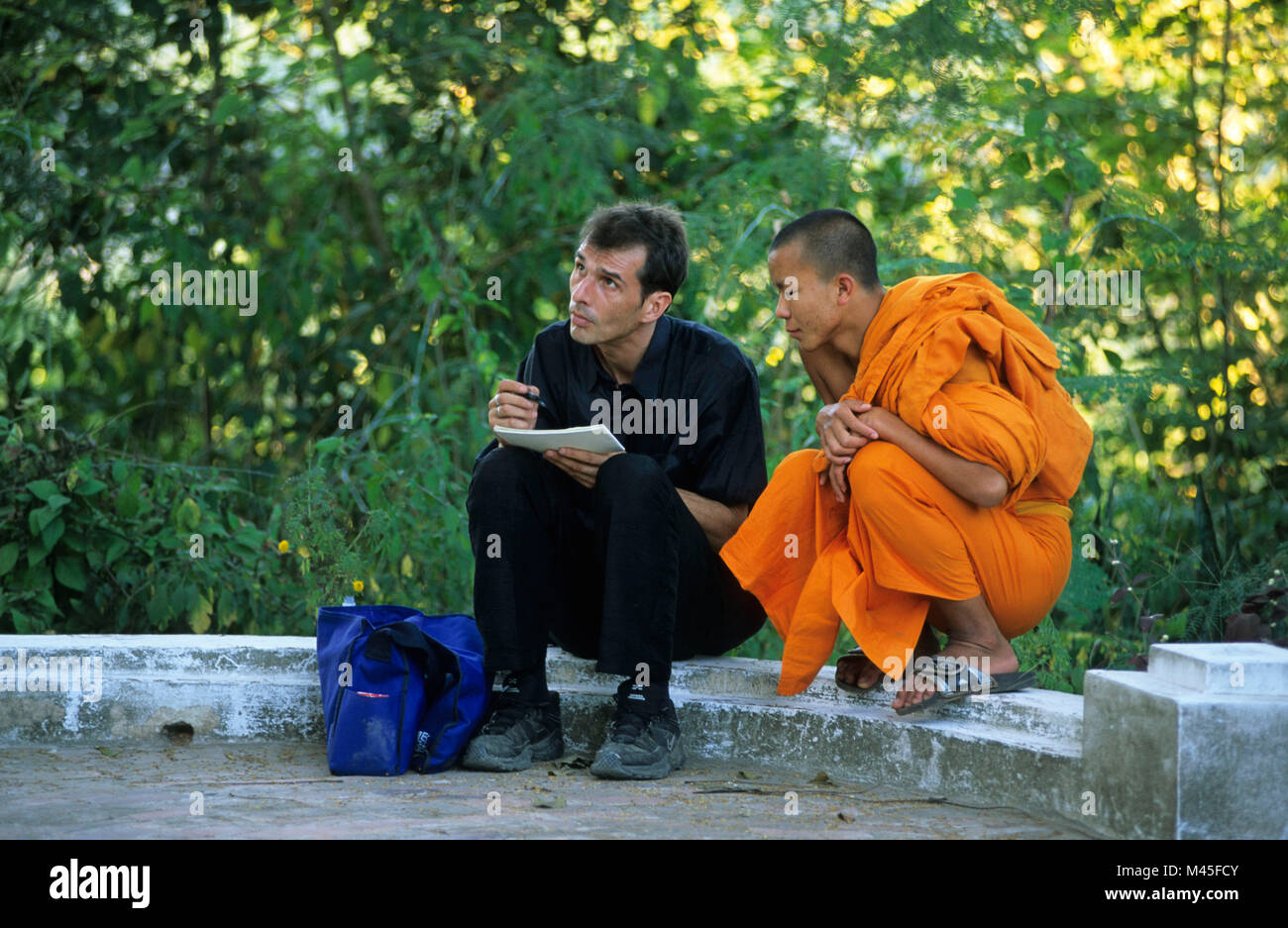 Laos. Luang Prabang. Wat Pha Phutthabaat buddhistischer Tempel. Buddhistischer Mönch sitzend mit Mann zu skizzieren. UNESCO-Weltkulturerbe. Stockfoto