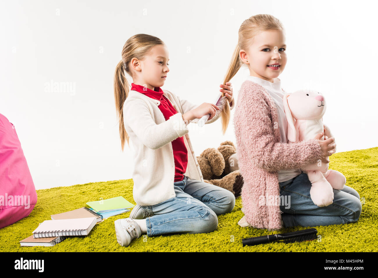 Schönes Kind bürsten Haare der Schwester, während Sie sitzen auf dem Boden mit stoffhäschen isoliert auf weißem Stockfoto