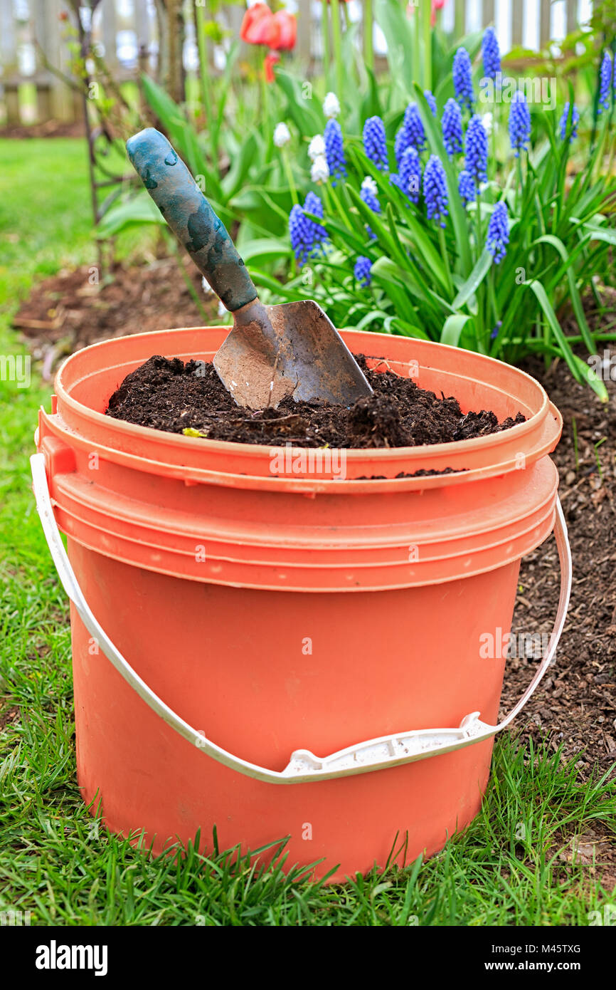 Ein Eimer voller Kompost mit einem Garten Kelle im heimischen Garten. Stockfoto