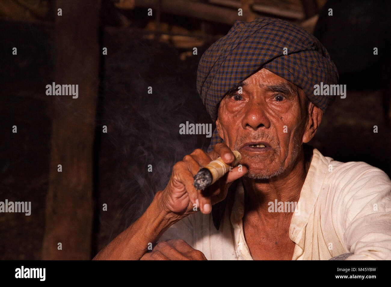 Lokale burmesische Mann rauchen Zigarre durch Feuer in seinem Haus in Bagan Myanmar Stockfoto