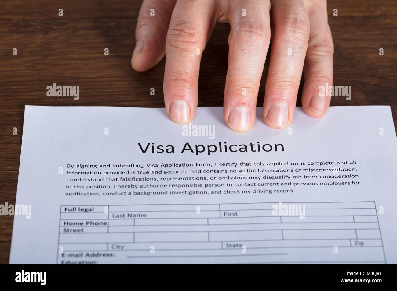 Hohe Betrachtungswinkel der Person Hand auf Visa Application Form an den hölzernen Schreibtisch Stockfoto