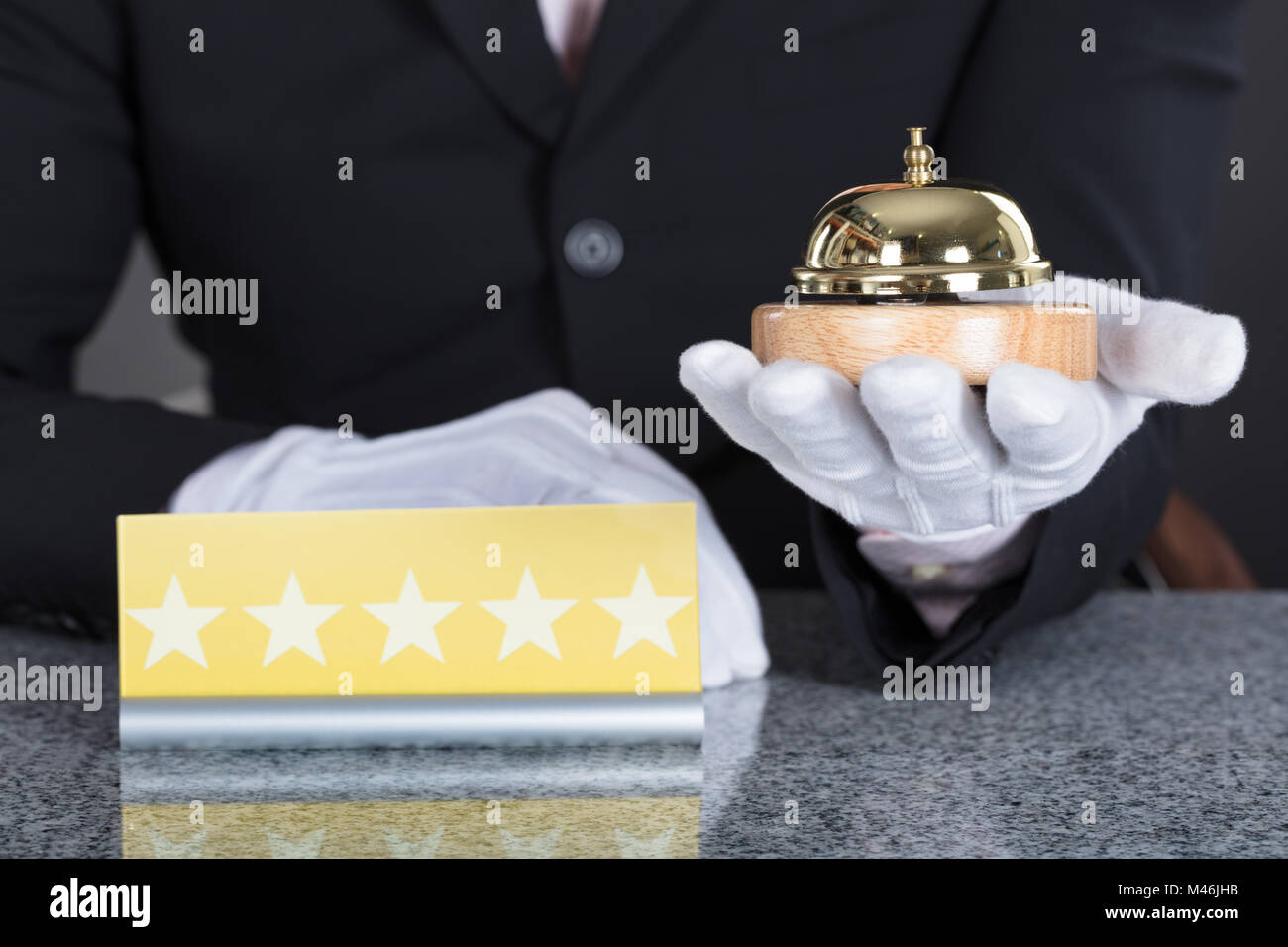 Nahaufnahme von einem Kellner Hand Holding Service Bell und fünf Stern Karte auf Schreibtisch Stockfoto