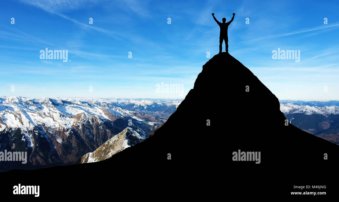 Die Silhouette eines Mannes, der die Hand beim Stehen an der Spitze der Berge im Winter Stockfoto