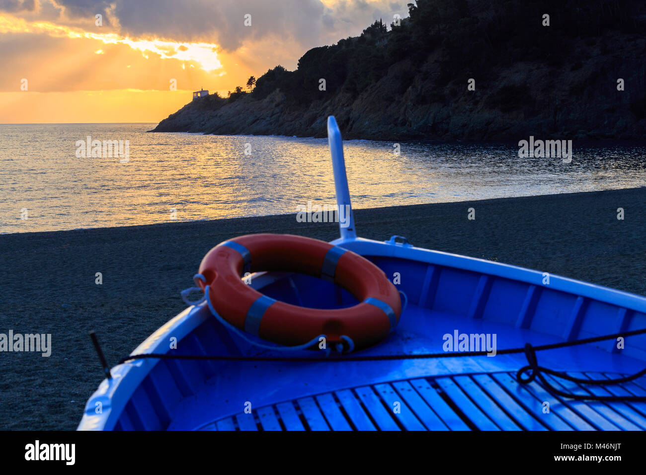 Boot auf den Strand von Bonassola mit Sonnenuntergang auf Madonnina della Punta Kirche. Loano, Ligurien, Italien. Stockfoto