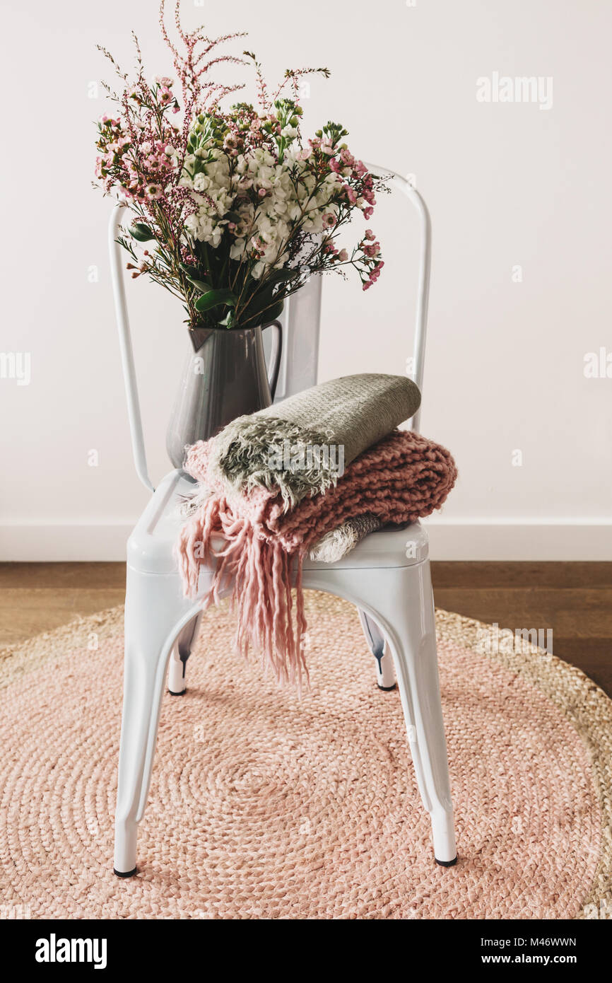 Rustikal Eingerichteten Vase mit Blumen mit Wolle Schals auf einem weißen Stuhl Stockfoto