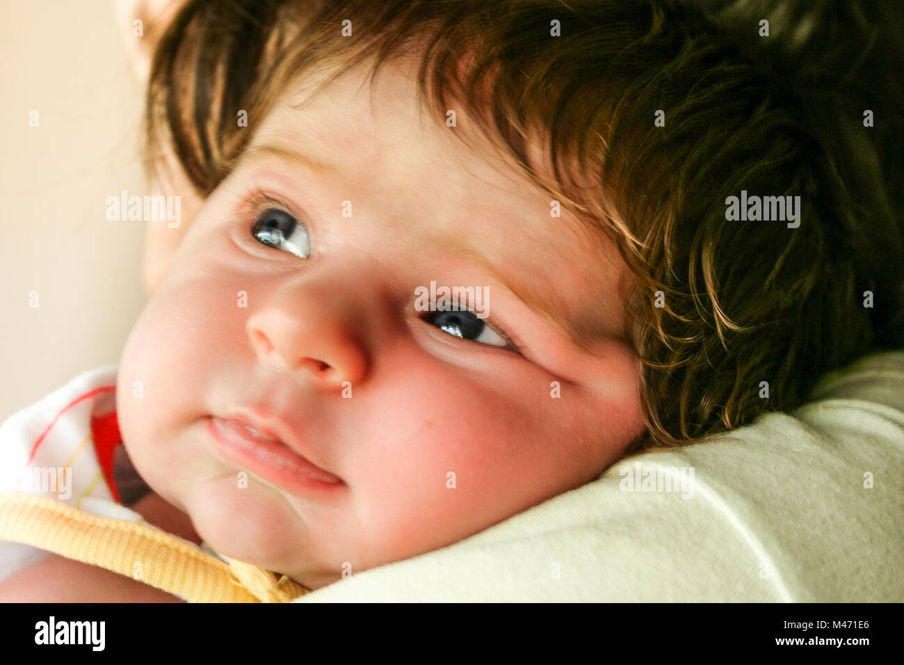 Ehrliches Porträt eines schönen einen Monat altes Baby lehnte sich auf der Schulter der Mutter; Licht in den Augen widerspiegelt Stockfoto