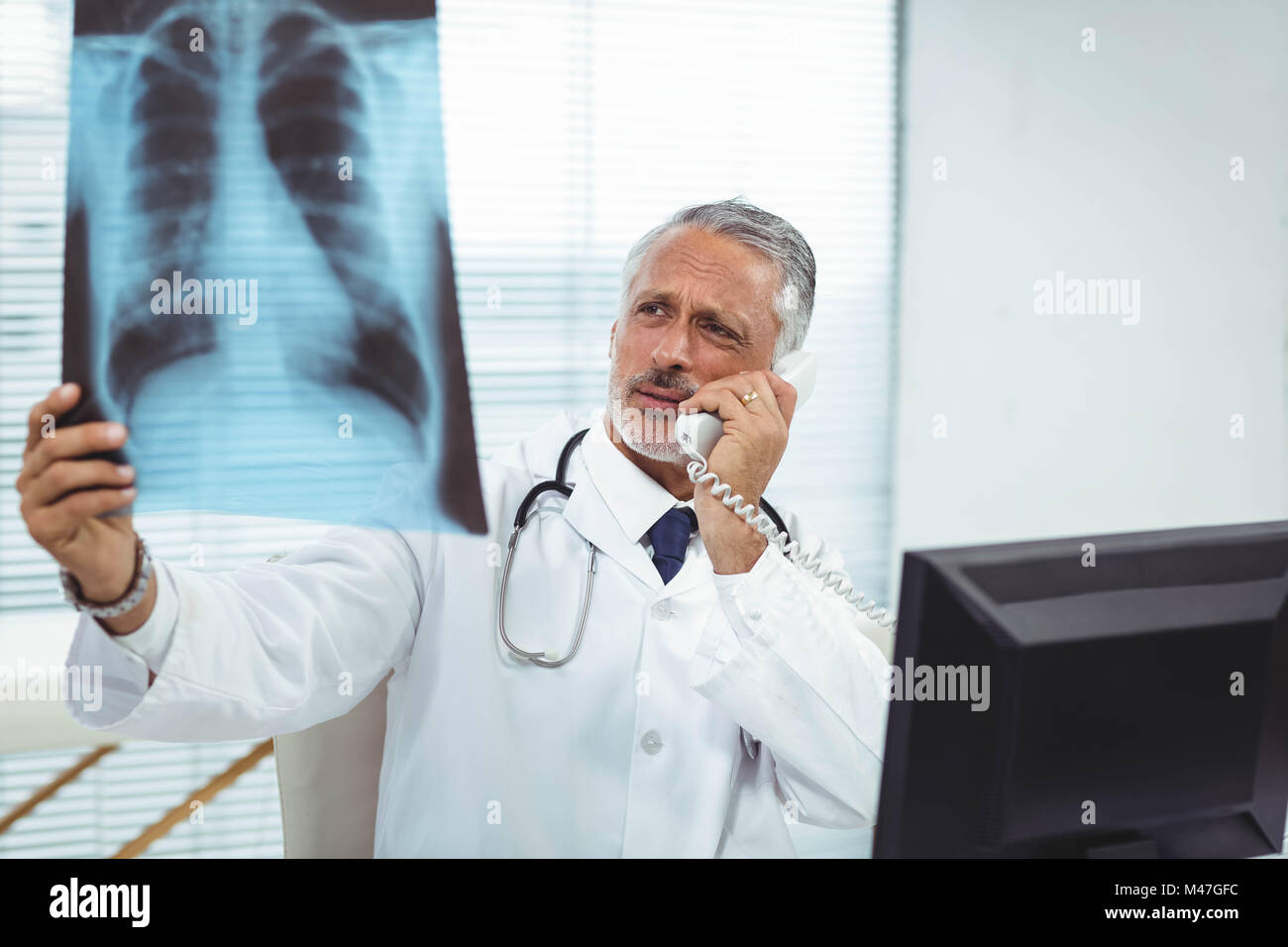 Arzt, Röntgen-Bericht während des Gesprächs am Telefon prüfen Stockfoto