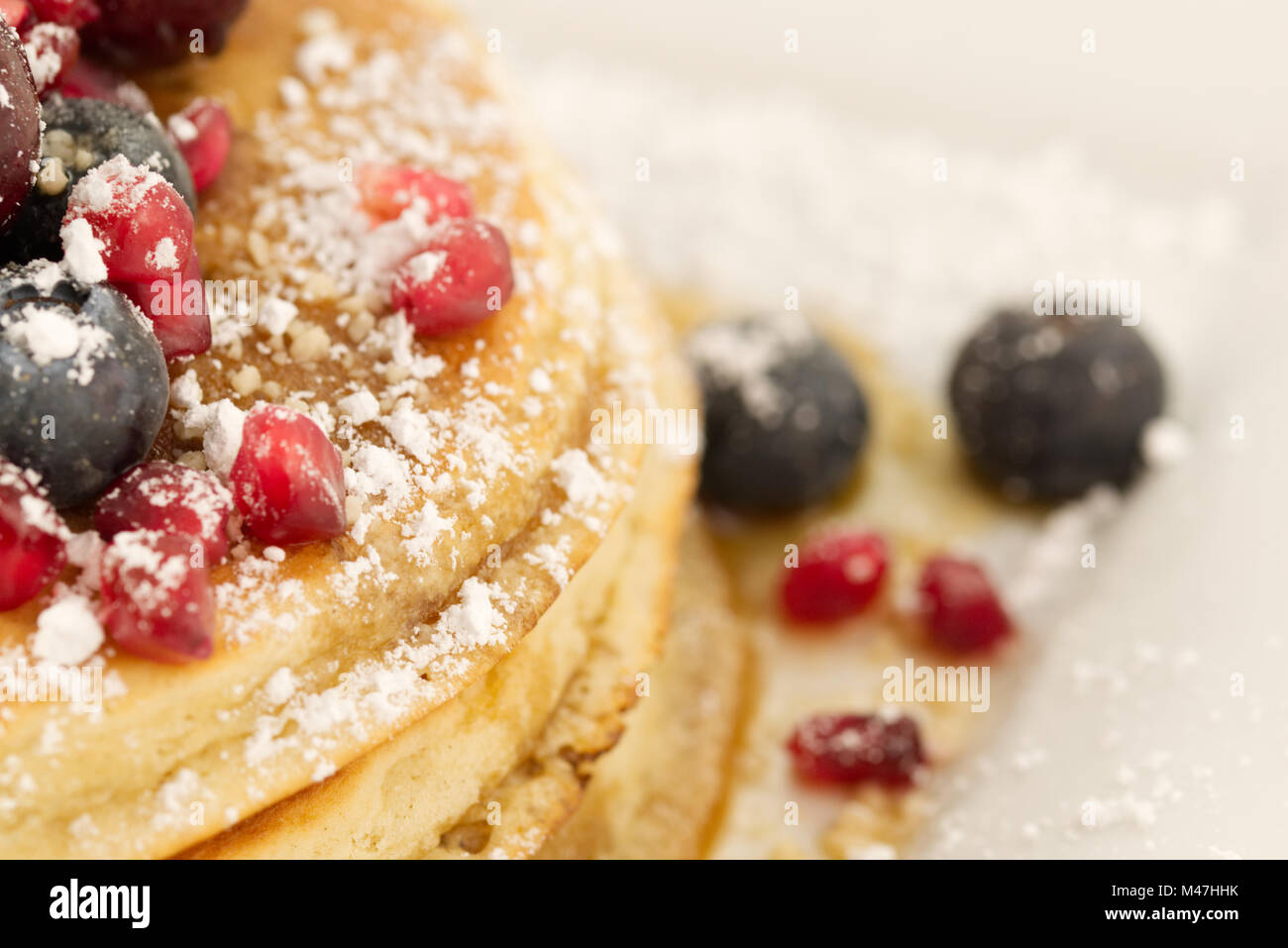 Frühstück Pfannkuchen mit Heidelbeeren, Granatapfel Samen, Kirschen und Puderzucker (staubzucker) und Ahornsirup auf weißem Hintergrund. Stockfoto