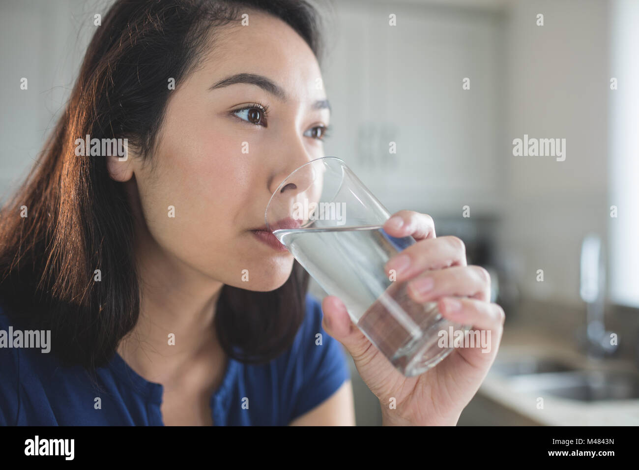 Junge Frau trinkt ein Glas Wasser in Küche Stockfoto