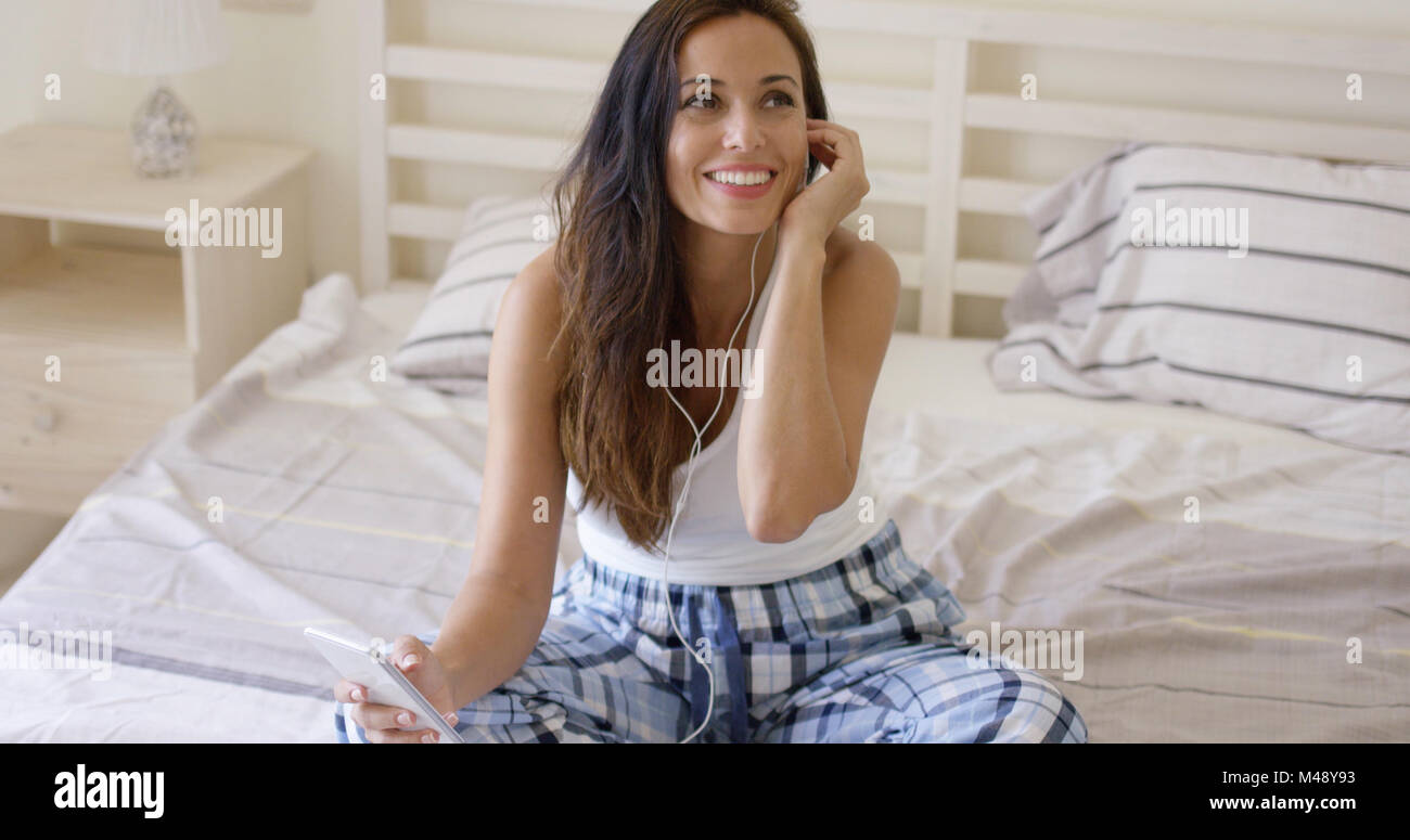 Lachende Frau mit Gerät mit Ohrhörer im Bett Stockfoto