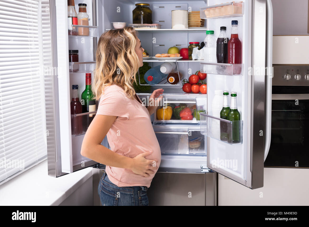 Junge schwangere Frau auf der Suche nach Essen im Kühlschrank Stockfoto
