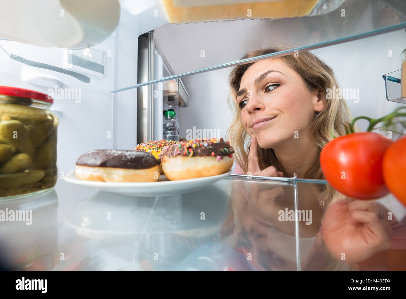Nahaufnahme eines verwirrten jungen Frau auf Donuts in offenen Kühlschrank Stockfoto