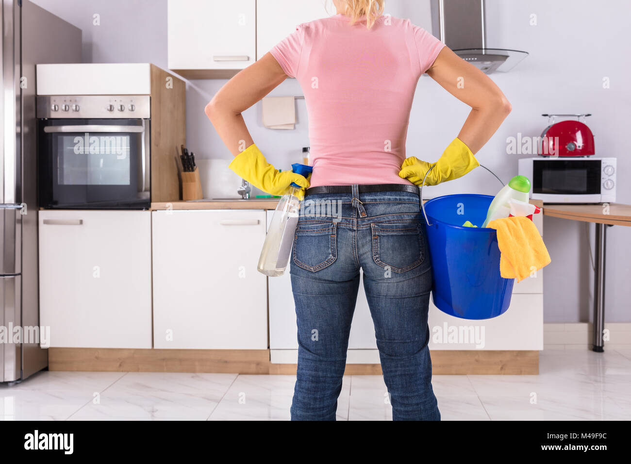 Ansicht der Rückseite Frau mit Reinigung von Werkzeugen und Produkten im Eimer in der Küche Stockfoto