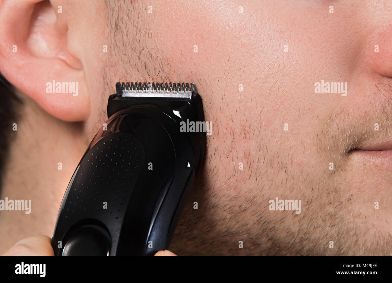 Trimmer auf Unrasierten Gesicht Nahaufnahme. Mann Rasieren mit dem elektrischen Rasierer. Stockfoto