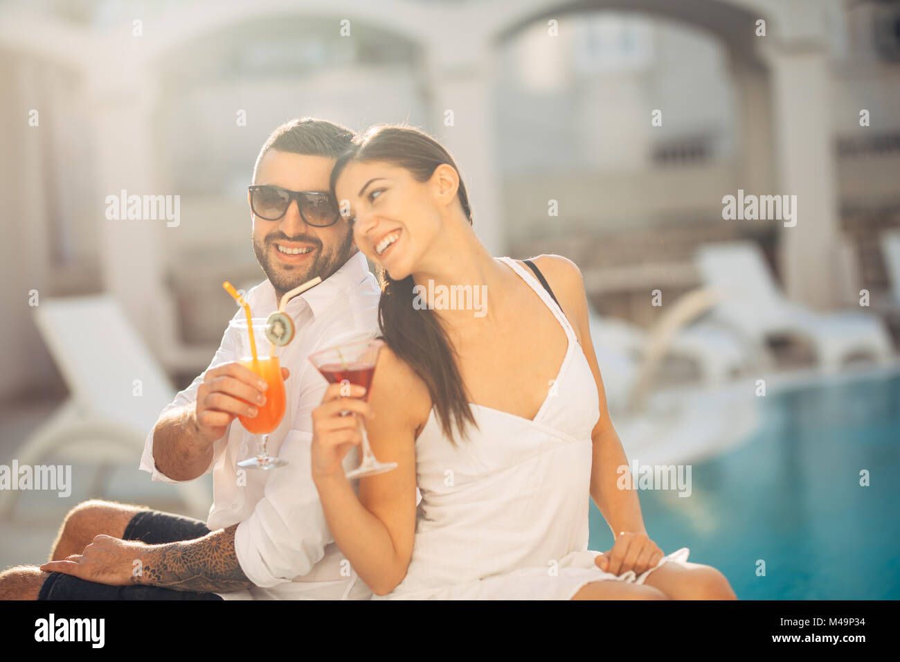 Youbg fröhliche liebenden Paar Cocktails am Pool im Sommer Urlaub. romantischen Abend in Luxus Resort. Feiern Liebe, Engagement, anniversar Stockfoto