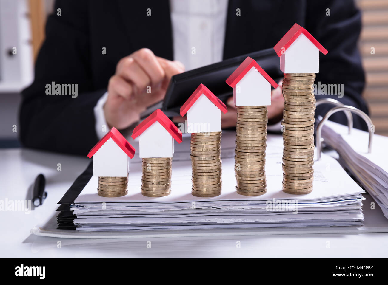 Mittelteil der Geschäftsfrau Berechnung Rechnung mit Haus Modelle arrangiert auf Gestapelte Münzen Stockfoto