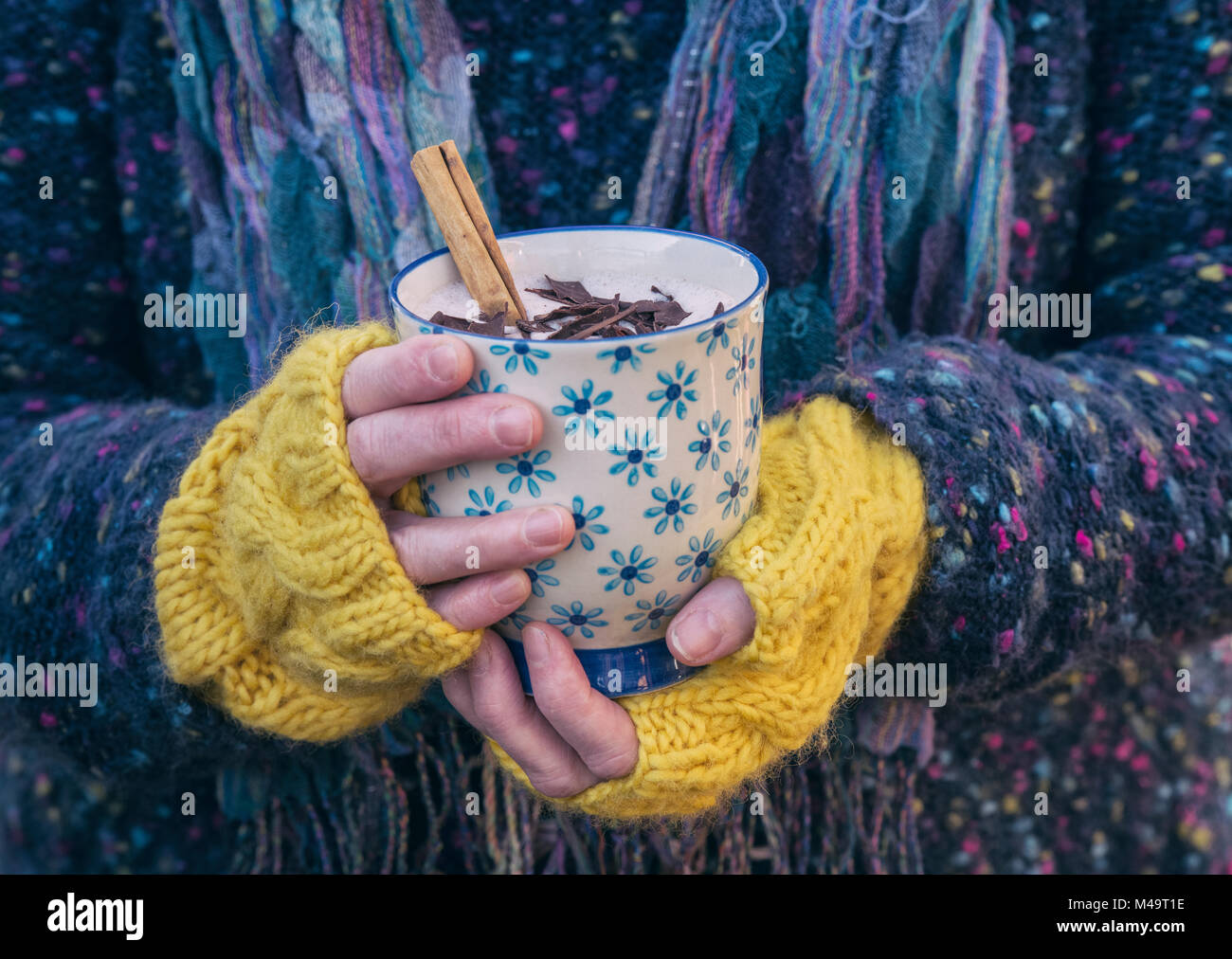 Womans Hände mit gelben woollen Handschuhe halten einer Tasse heißer Schokolade mit einer Zimtstange und dunkler Schokolade Spänen Stockfoto