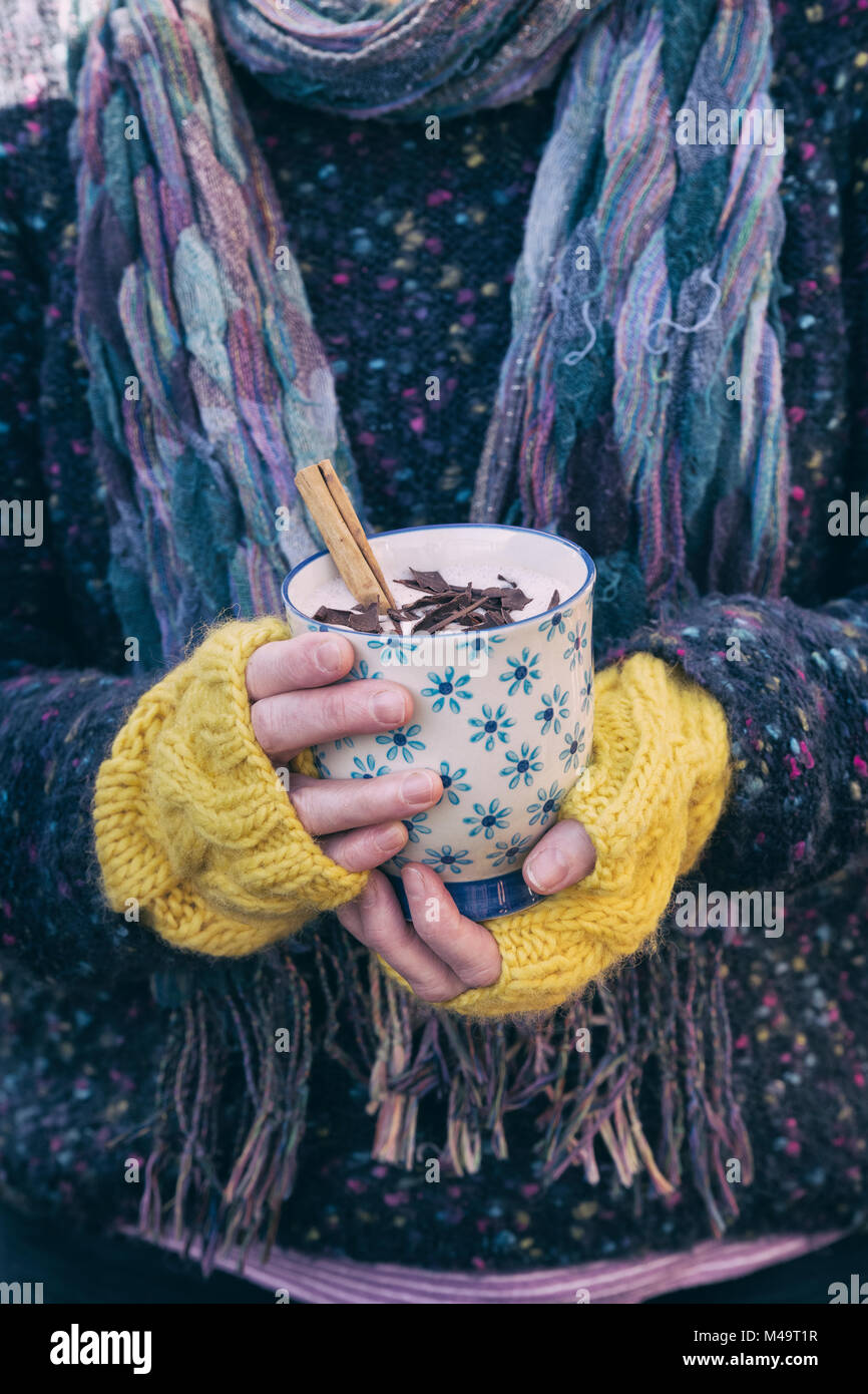 Womans Hände mit gelben woollen Handschuhe halten einer Tasse heißer Schokolade mit einer Zimtstange und dunkler Schokolade Spänen Stockfoto