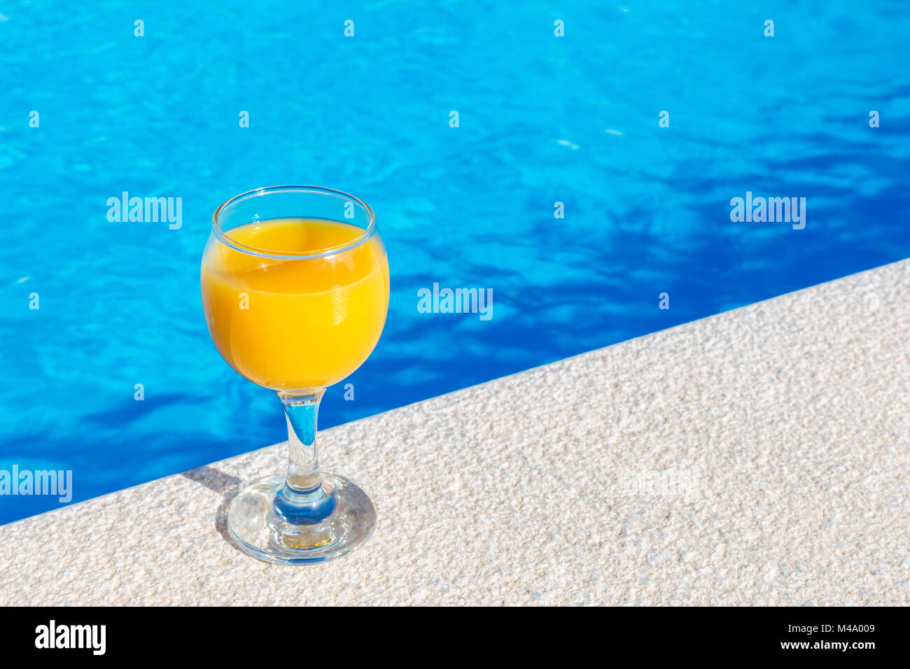 Glas mit Orangensaft am Rand des Pools Stockfoto