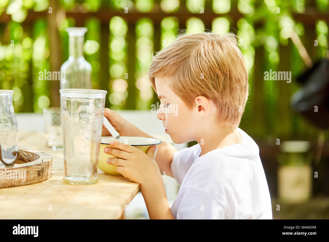Kleine junge isst Müsli zum Frühstück im Garten im Sommer und schmollt Stockfoto