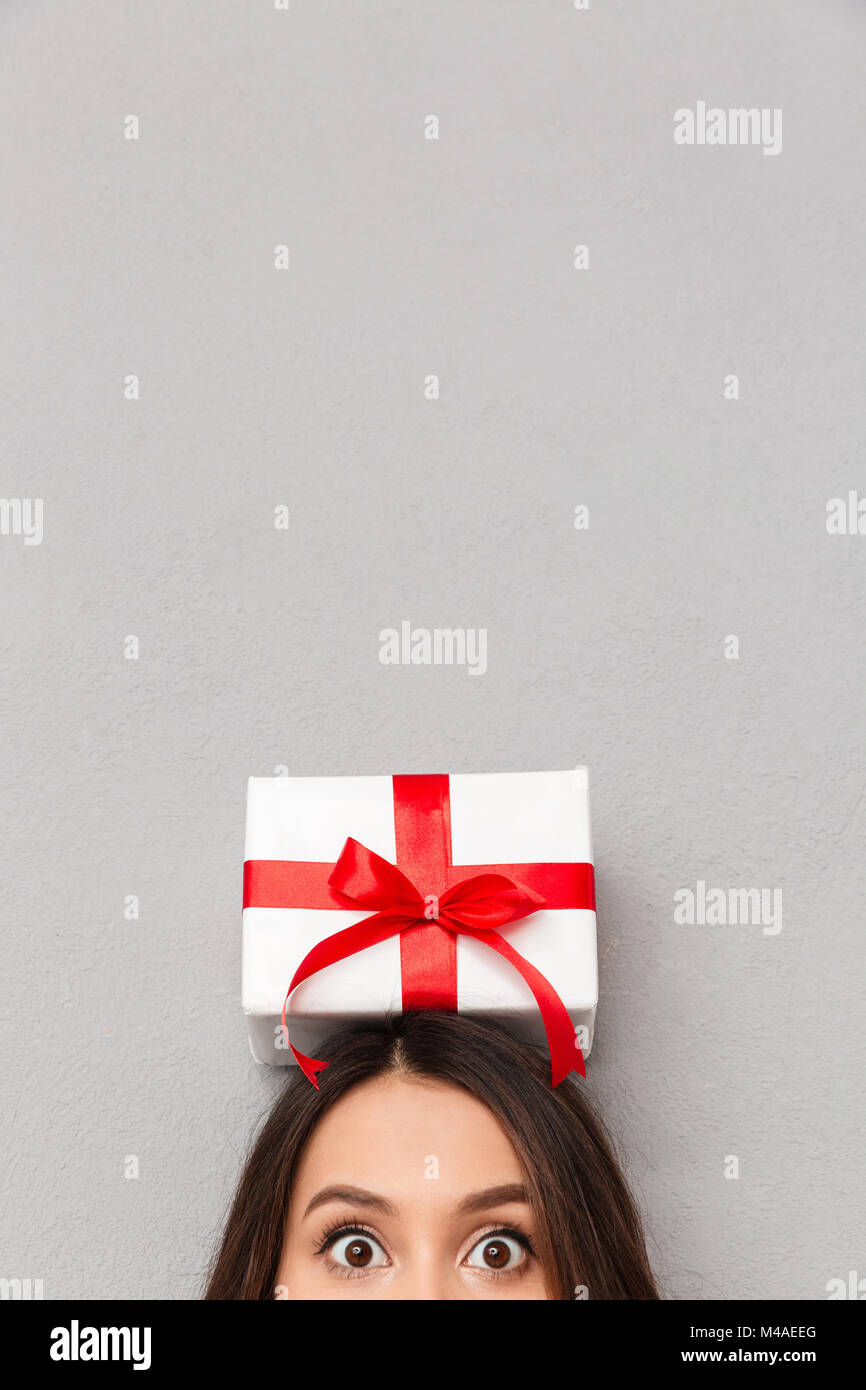 Lustig Bild des kühlen Frau Ausbauchende Augen und posiert mit Bithday Geschenk mit roter Schleife auf dem Kopf, isoliert über grauer Hintergrund posiert Stockfoto