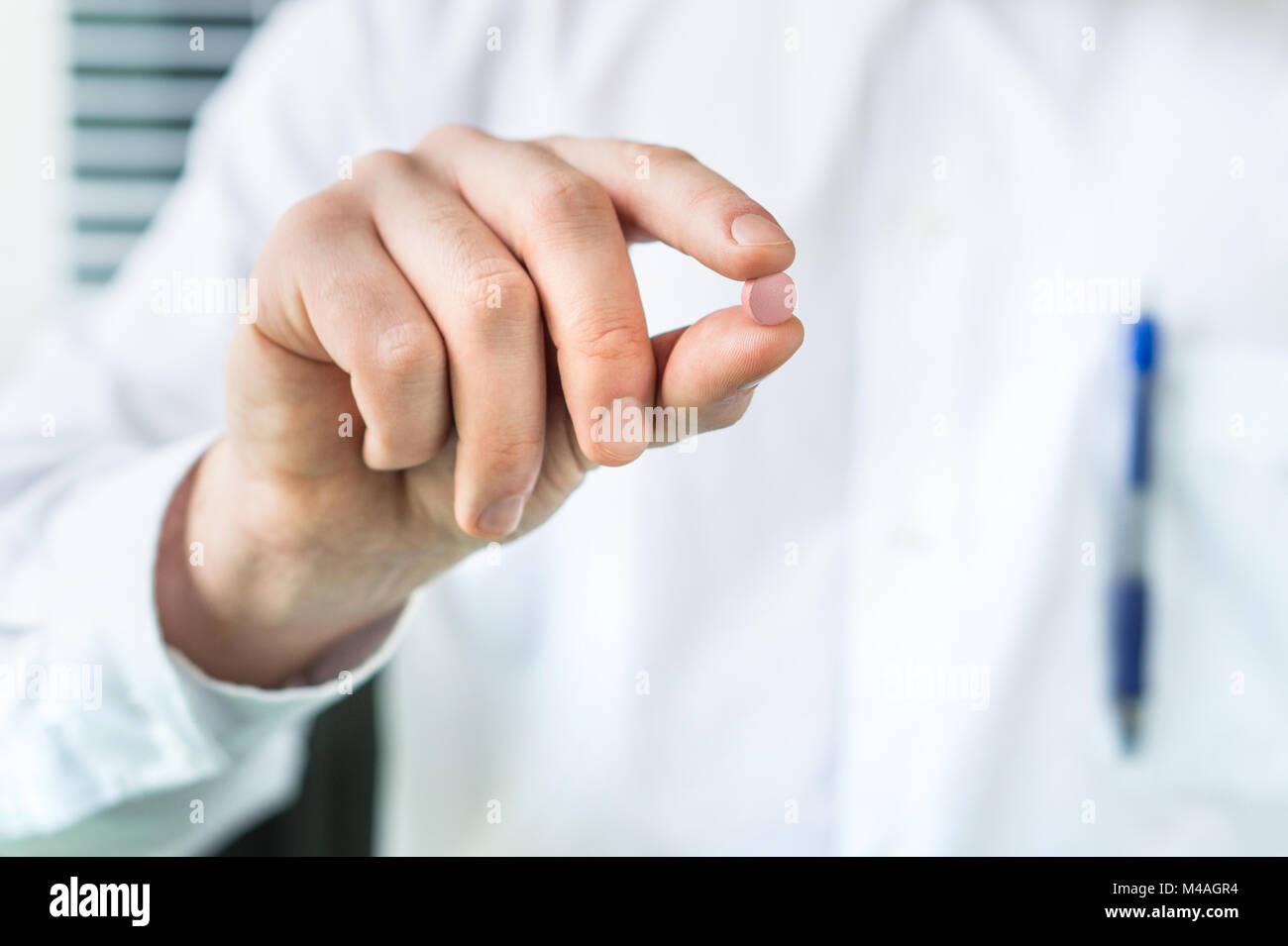 Arzt oder Apotheker Holding eine Pille zwischen den Fingern. Arzt und Experte im weißen Mantel mit Medizin. Stockfoto
