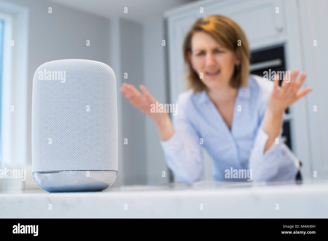 Frustrierte Frau in der Küche Fragen Digital Assistant Frage Stockfoto