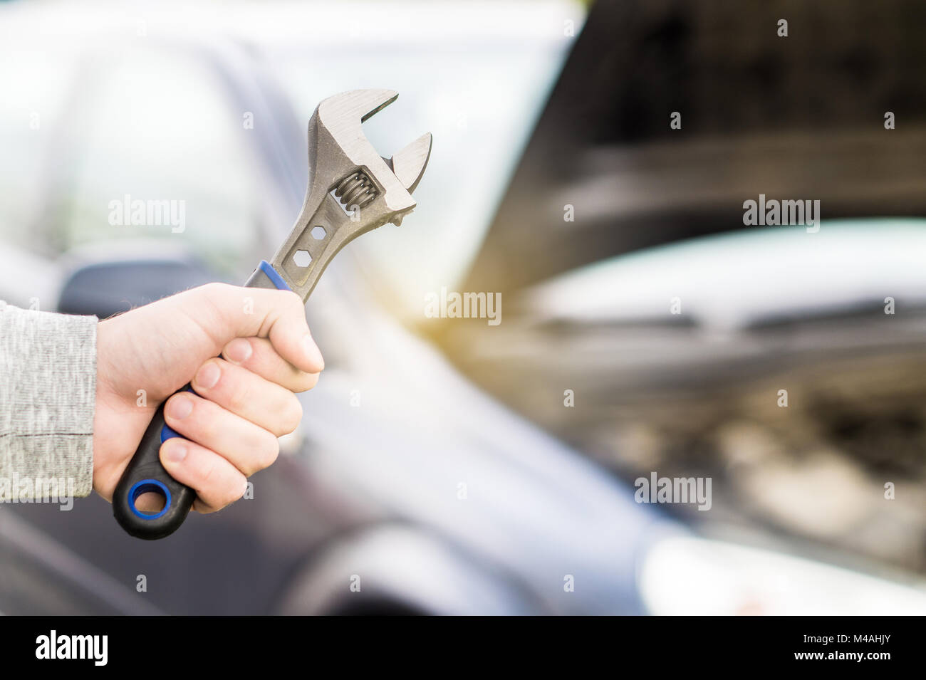 Auto Reparatur, Wartung und Inspektion Konzept. Mann mit Schraubenschlüssel vor einem Auto mit unter der Haube und Motor. Stockfoto