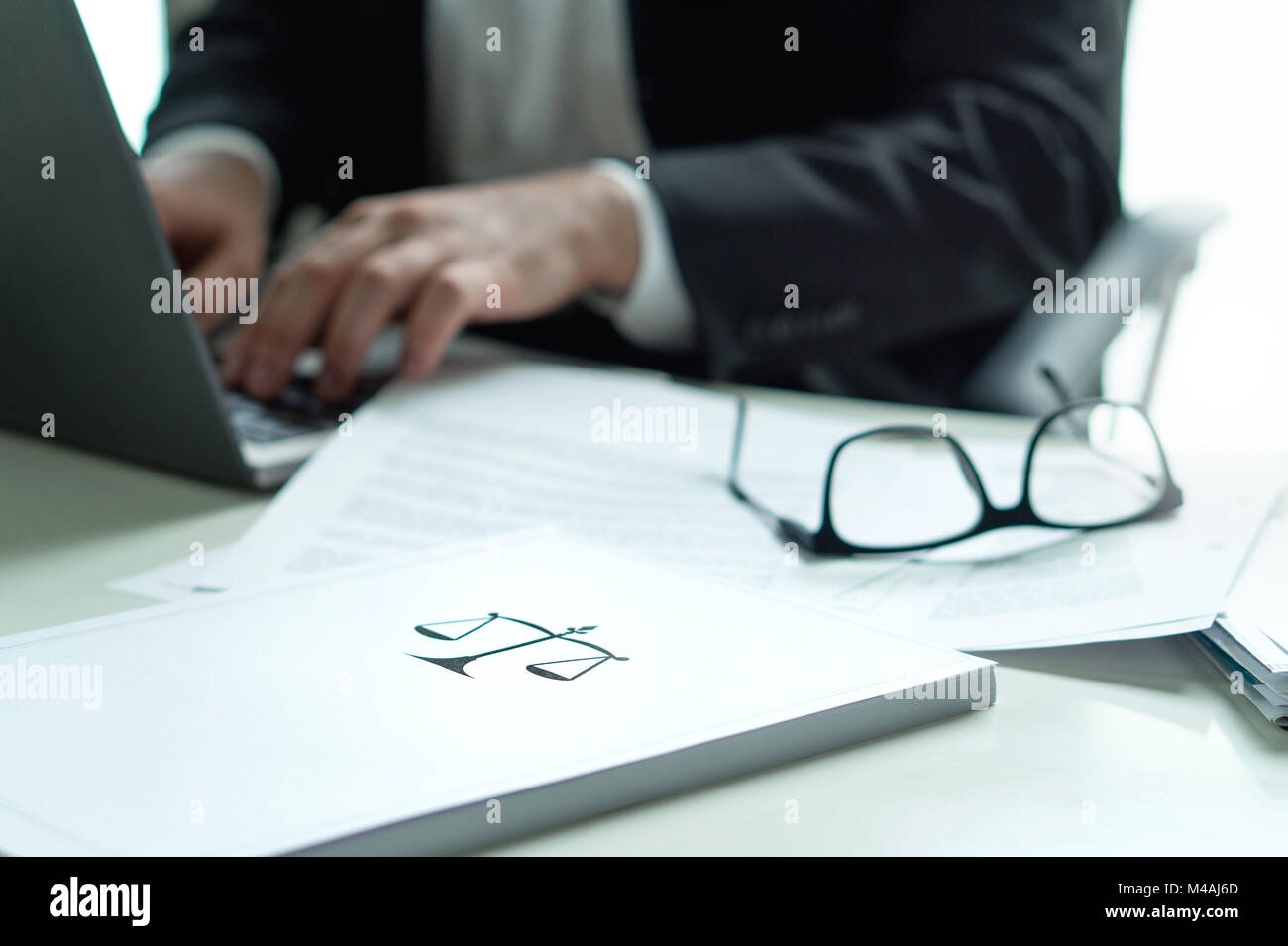 Rechtsanwalt im Büro. Rechtsanwalt schreiben ein juristisches Dokument mit Laptop. Gläser auf dem Tisch. Stapel Papier mit Skala und Gerechtigkeit Symbol. Stockfoto