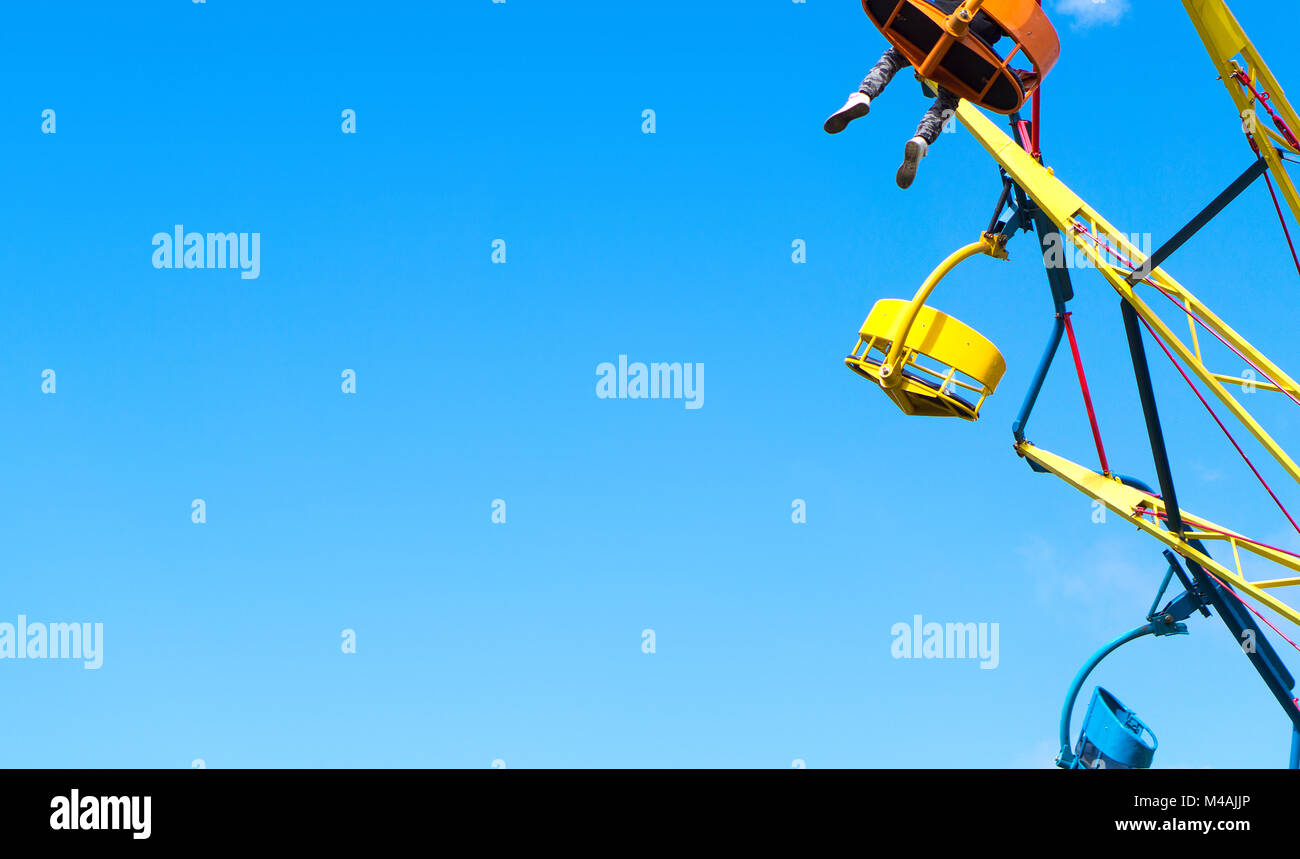 Vergnügungspark Hintergrund Vorlage mit negativen kopieren. Bunte Theme Park Fahrt gegen den klaren, blauen Himmel im Sommer. Eine Person mit Beinen hängen. Stockfoto Vergnügungspark Hintergrund Vorlage mit negativen kopieren. Bunte Theme Park Fahrt gegen den klaren, blauen Himmel im Sommer. Eine Person mit Beinen hängen. Stockfoto