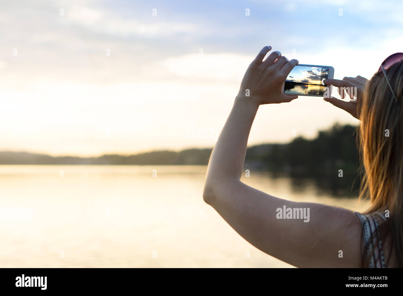 Junge Frau mit Foto von einem schönen Sonnenuntergang mit Smart Phone. Sorglosen Sommerurlaub Lebensstil. Reisen und Freizeit Konzept. Stockfoto