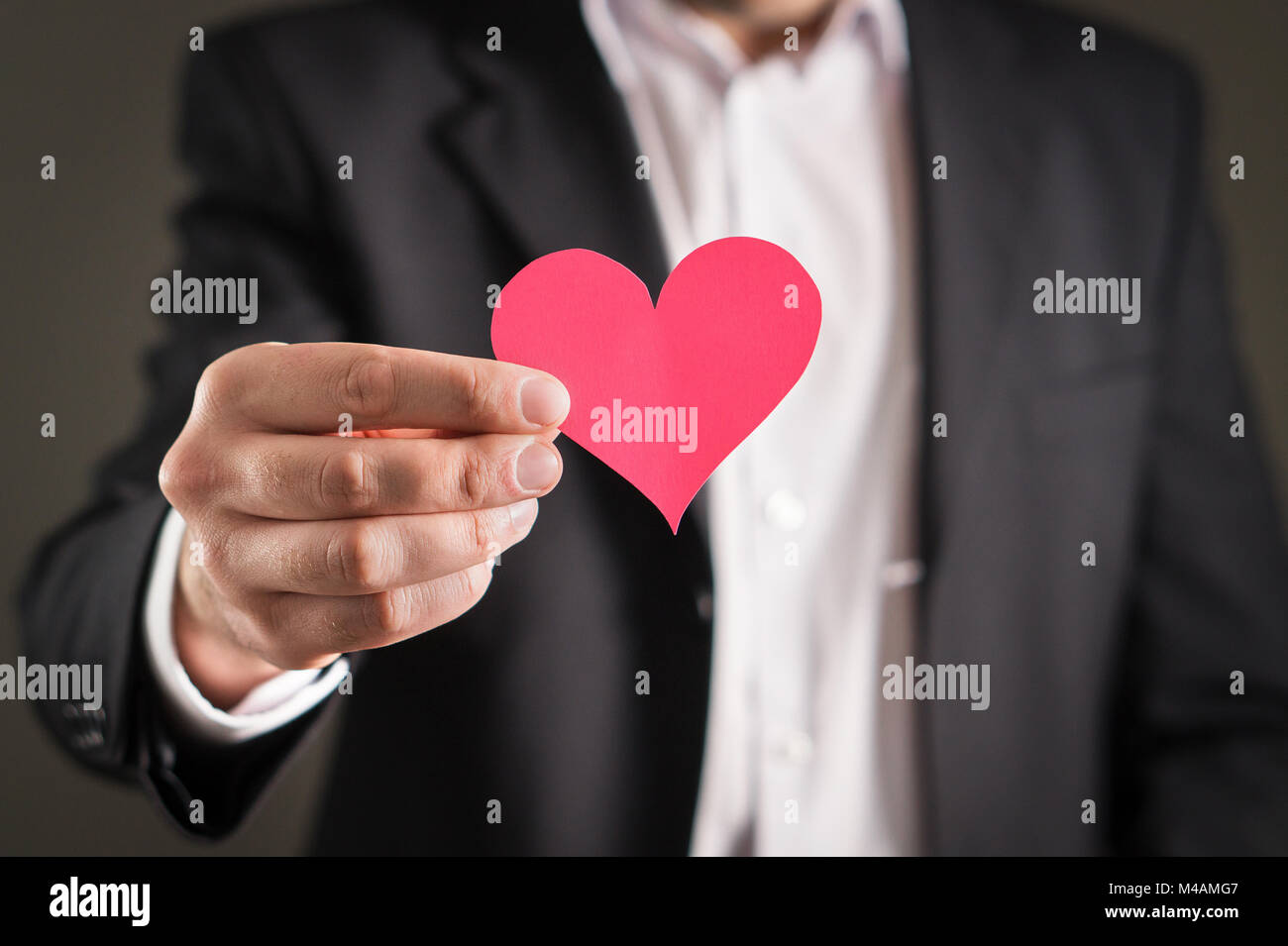 Mann in Anzug und einen Karton Papier Herzen. Geschäftsmann oder Verlobten mit einer Liebe Symbol. Vorschlag, Hochzeit, dating oder Valentinstag Konzept. Stockfoto