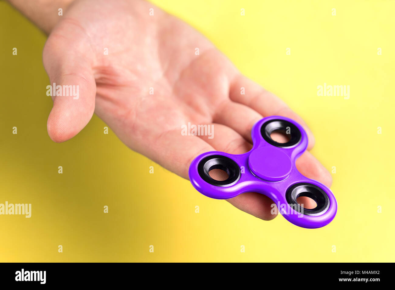 Lila und Violett zappeln Spinner an Hand, Handfläche und Finger gegen den gelben Hintergrund. Stockfoto