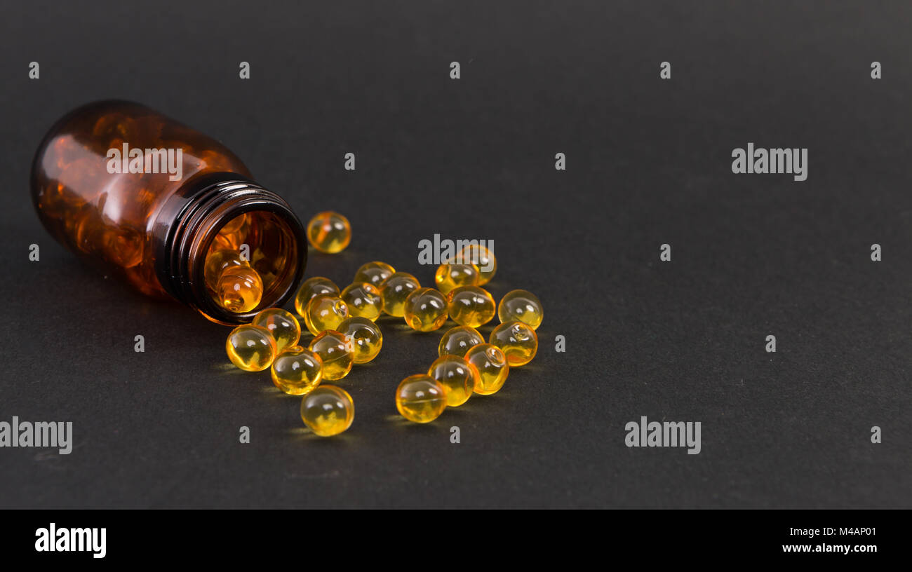 Verschüttete gelb transparent goldenen Kapseln Vitamin auf dunklem Hintergrund, wie die Haut Behandlung Konzept Stockfoto