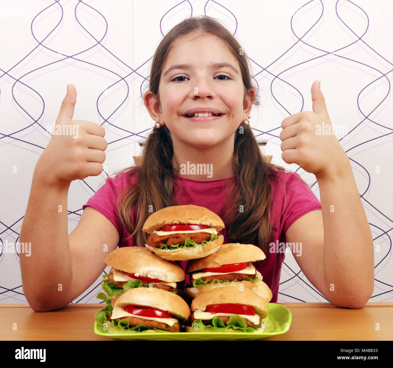 Glückliche kleine Mädchen mit Hamburger und Daumen hoch Stockfoto