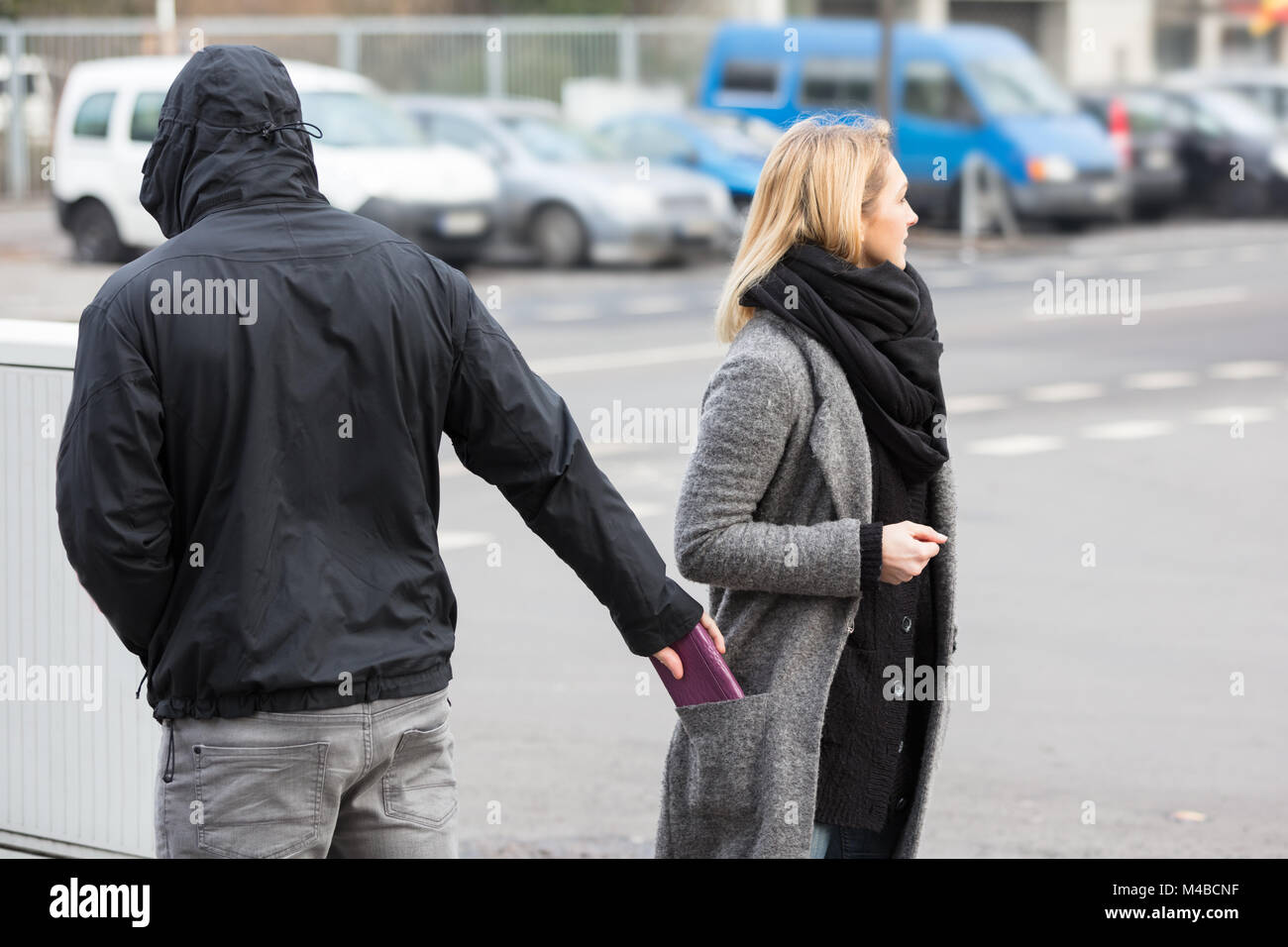 Mann in einer Haube Diebstahl Geldbörse aus der Frau Jackentasche auf der Straße Stockfoto
