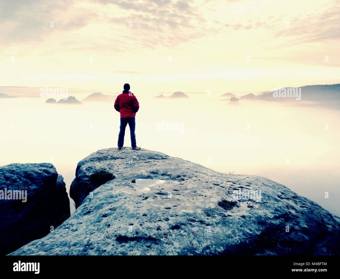 Mann bleibt auf einem Felsen über den Wolken. Mann auf dem Berg. Konzeption. Stockfoto