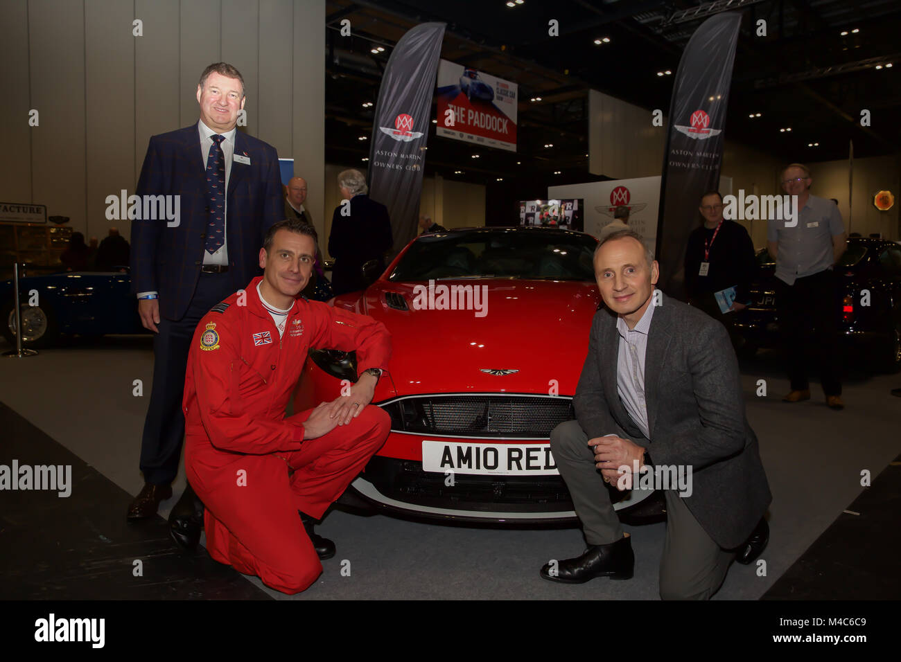 London, Großbritannien. 15 Feb, 2018. Glückliche Gewinner Humphrey Bradley stellt mit seinem Aston Martin Vanquish S rote Pfeile Auto mit roten Pfeilen pilot Squadron Leader Adam Collins (in Rot fliegenden Anzug), Rot 10 an der London Classic Car Show, Excel © Keith Larby/Alamy leben Nachrichten Stockfoto