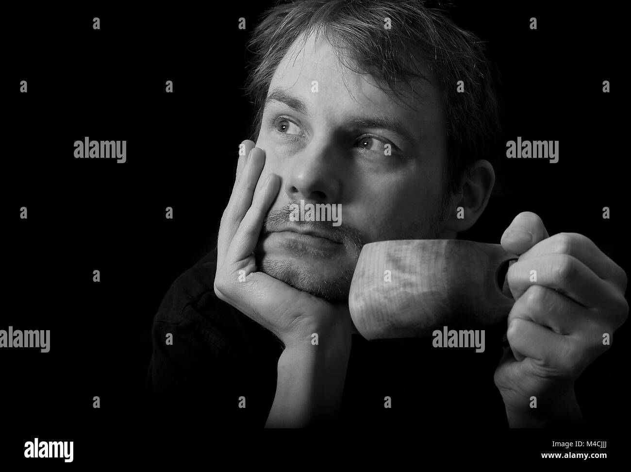 Junger Mann mit einem hölzernen Kaffee oder Tee Becher, der scheint zu Träumen oder in Gedanken verloren. Dunkle low-key-schwarz-weiß Foto im Hochformat. Stockfoto